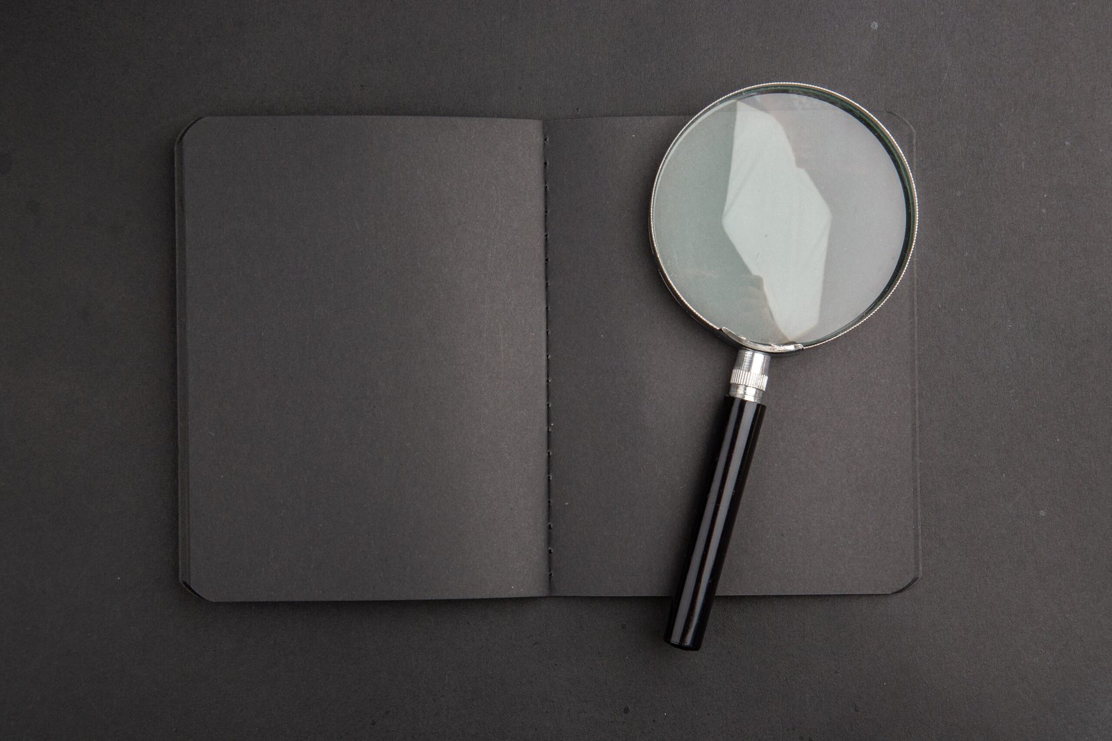 top-view-black-notebook-magnifying-glass-dark-table
